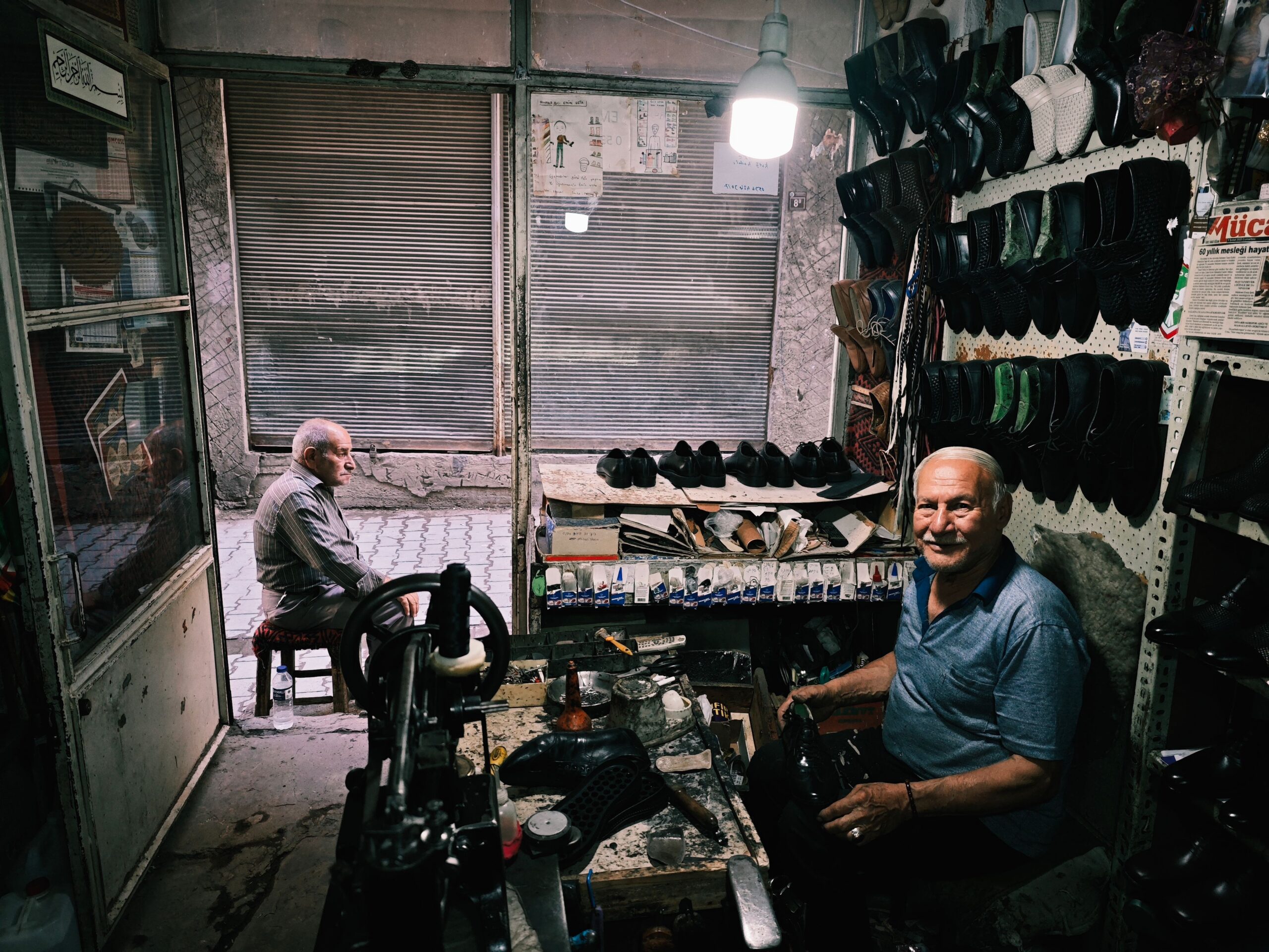 Topics & Knowledge Two cobblers in a Diyarbakır shop, surrounded by tools and shoes. Traditional craftsmanship.